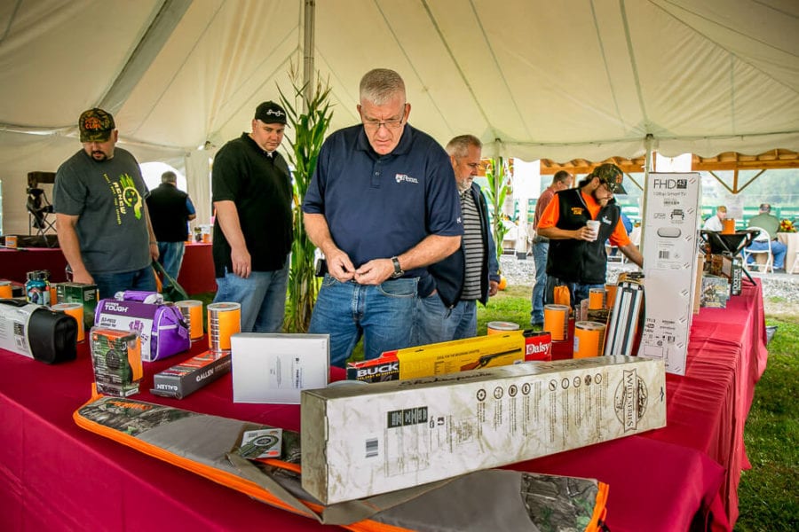 Men examining raffle prizes on table under tent