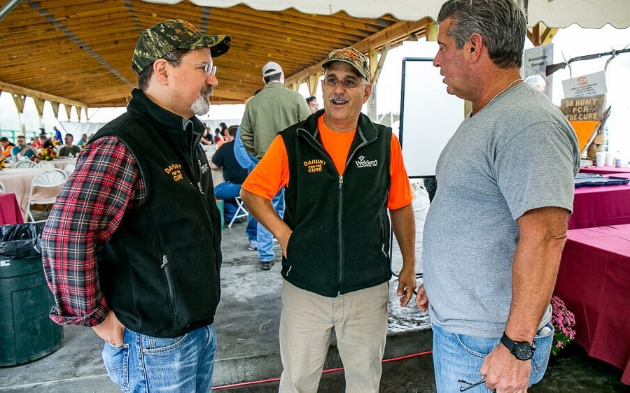 Three men talking under an event tent