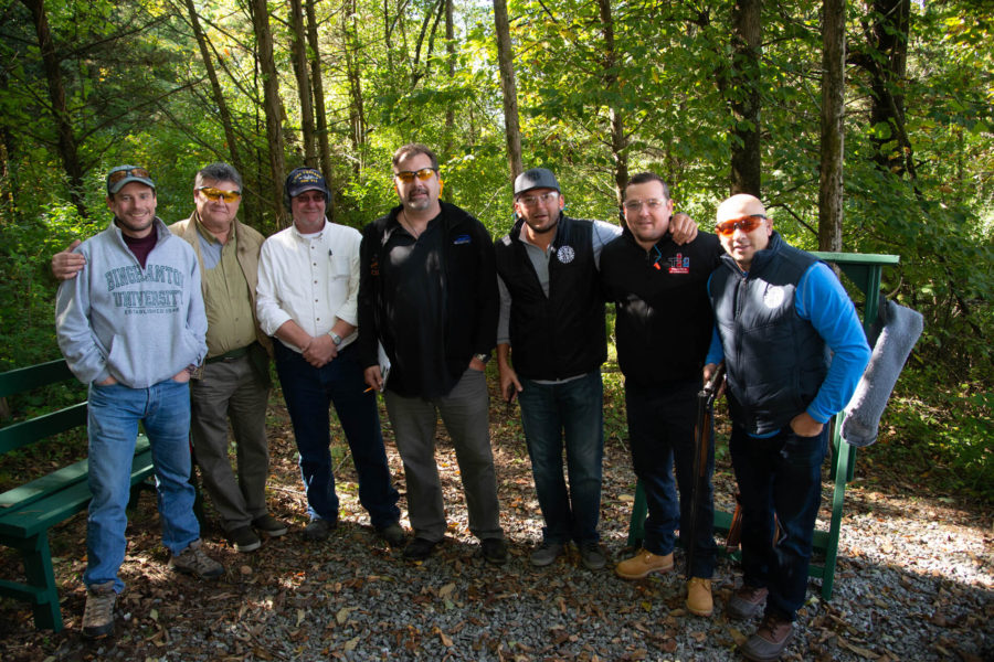 Seven men posing together in wooded area