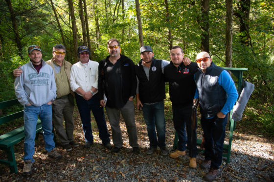 Group of seven men posing outdoors in woods