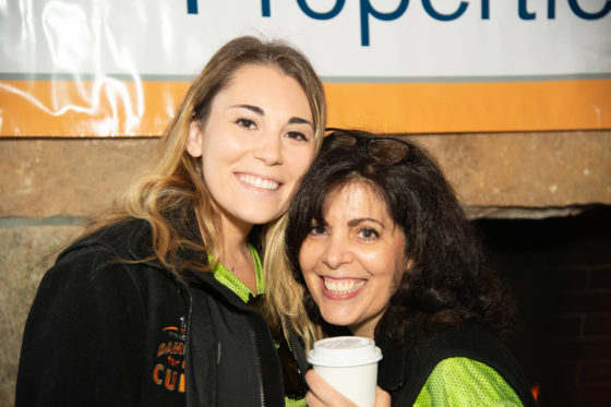 Two smiling women posing, one holding coffee