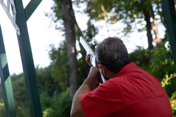Person aiming shotgun outdoors in wooded area