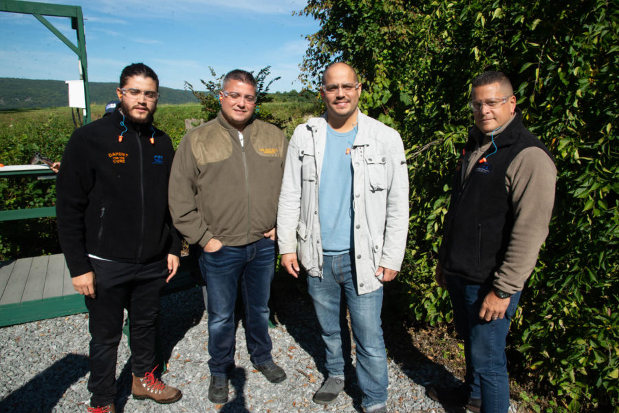 Four men standing outdoors near green foliage