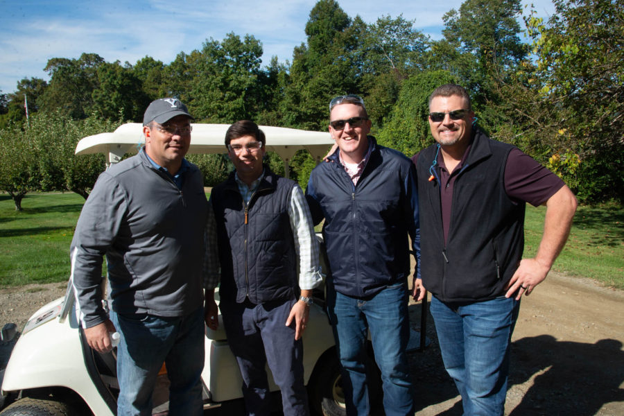 Four men posing by golf cart outdoors