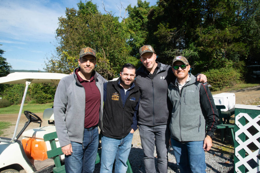 Four men smiling outdoors by golf cart