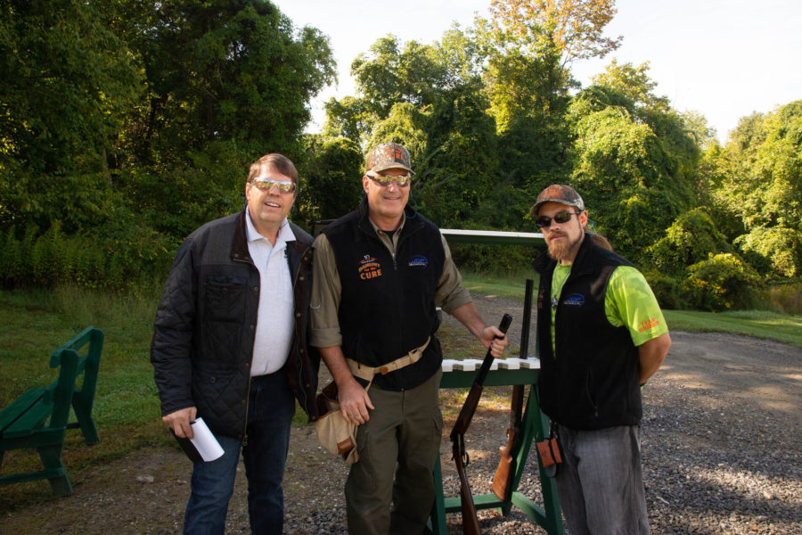 Three men posing with shotguns outdoors