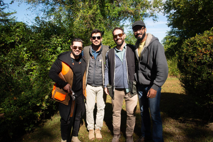 Four men outdoors posing with shotgun