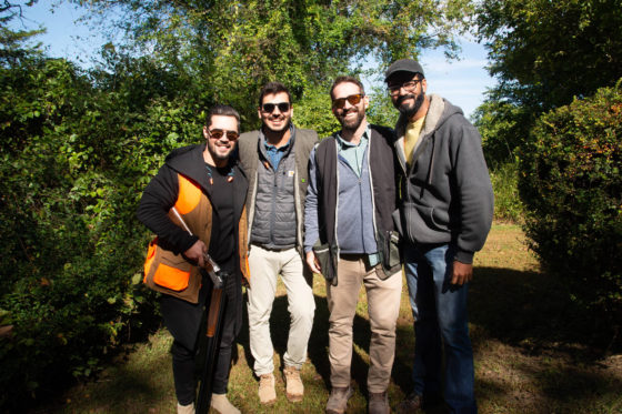Four men smiling outdoors, one with shotgun