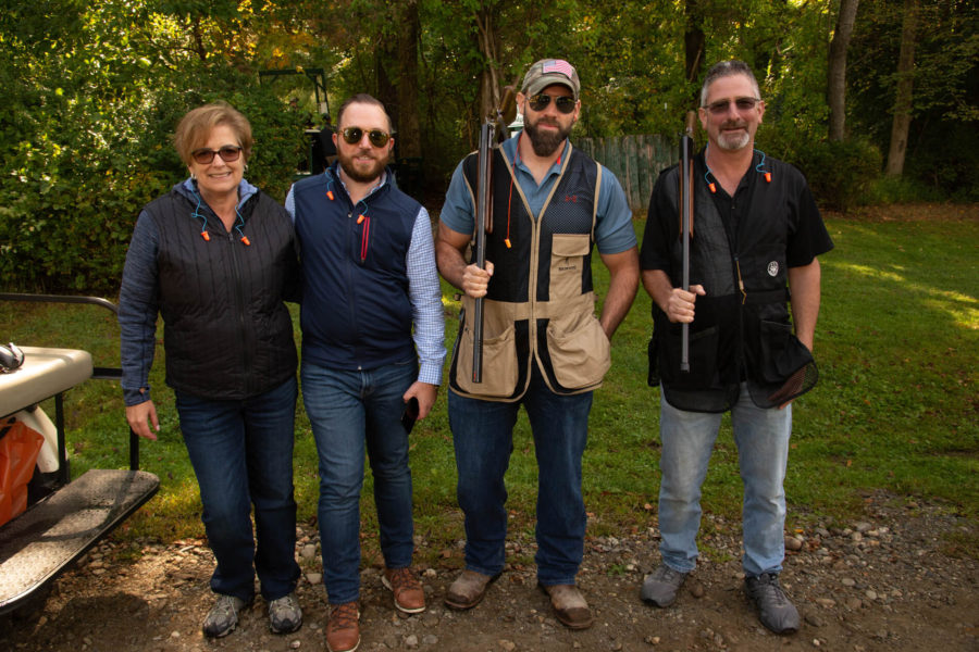 Four adults posing with shotguns outdoors