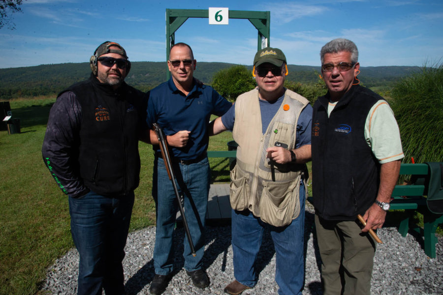 Four men posing at outdoor shooting range