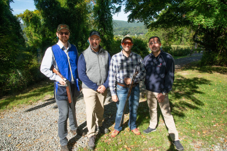 Four people posing outdoors with shotguns
