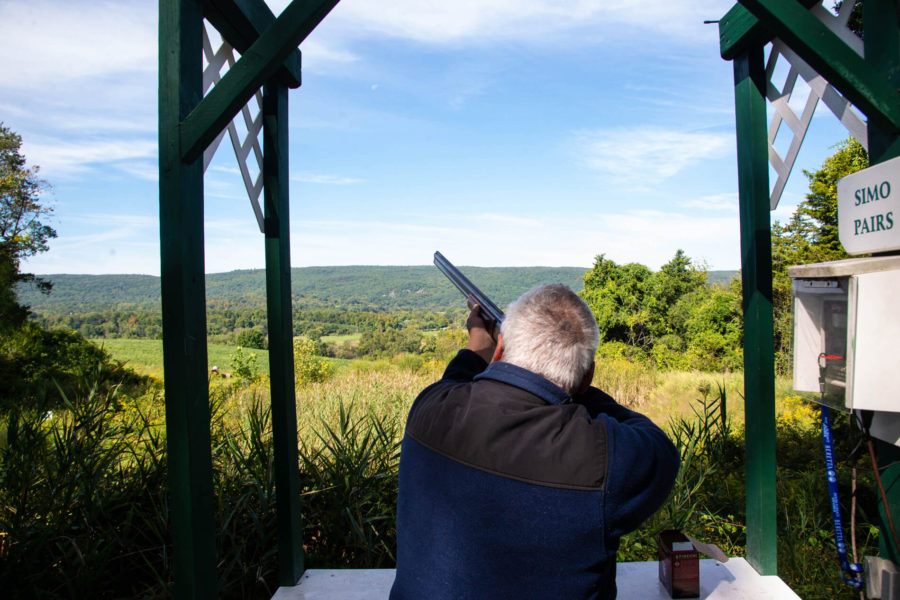Shooter aiming shotgun at outdoor clay target range