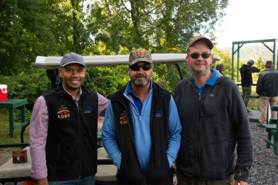 Three men smiling outdoors by golf cart