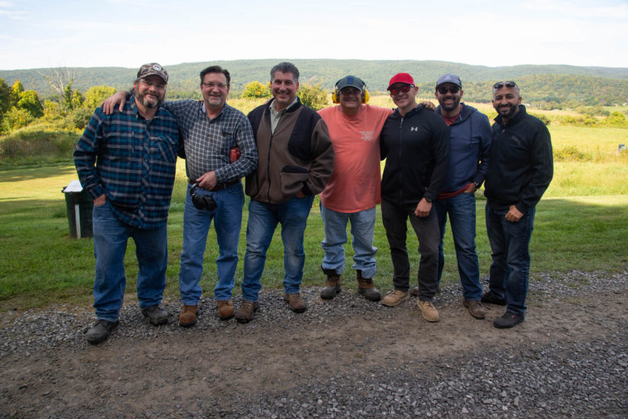 Seven men smiling outdoors with rolling hills