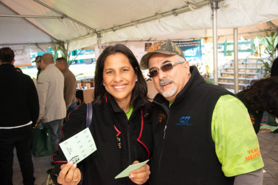 Two smiling people holding raffle tickets under tent