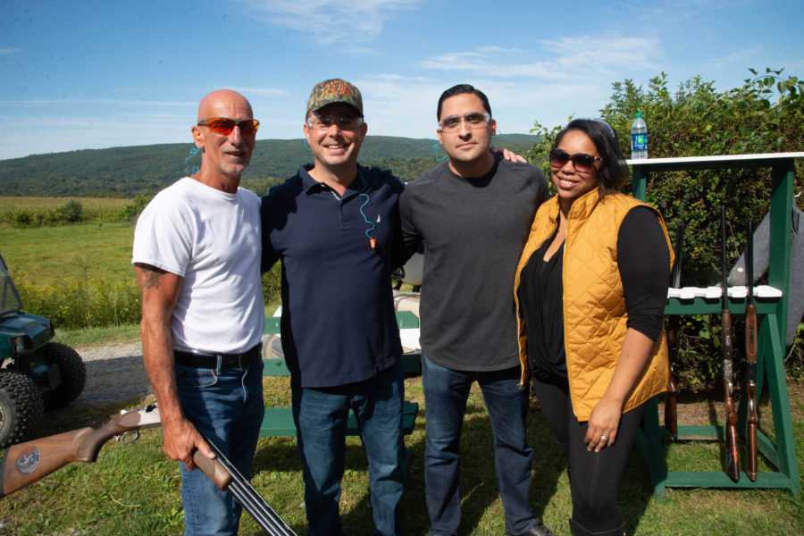 Group of four people posing outdoors with shotgun
