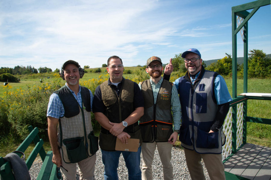 Four men wearing shooting vests at outdoor range