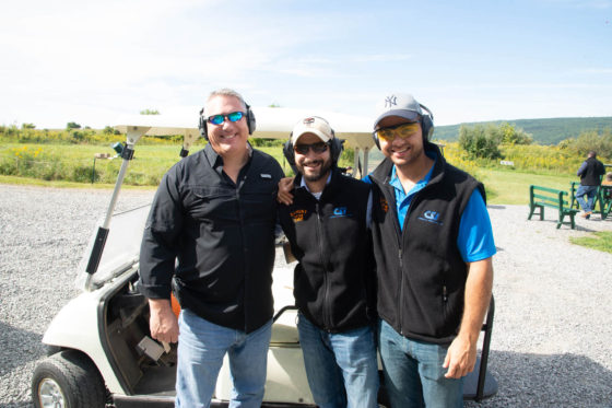 Three men wearing hearing protection by golf cart