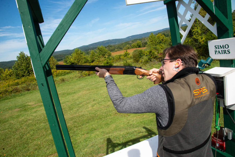 Shooter aiming shotgun at outdoor skeet range