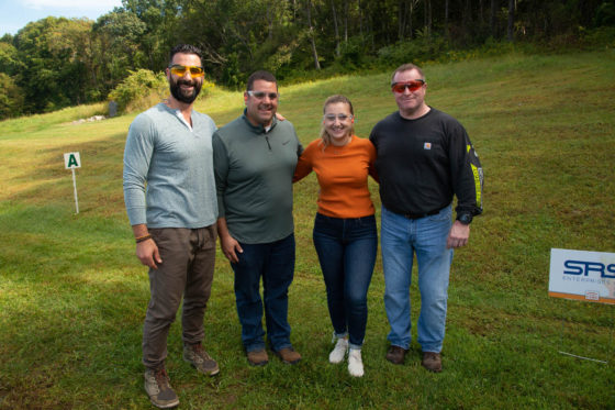 Four adults smiling outdoors on grassy hill