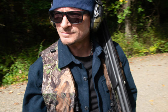 Man wearing camo vest carrying shotgun outdoors