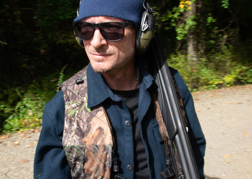 Man wearing camo vest carrying shotgun outdoors