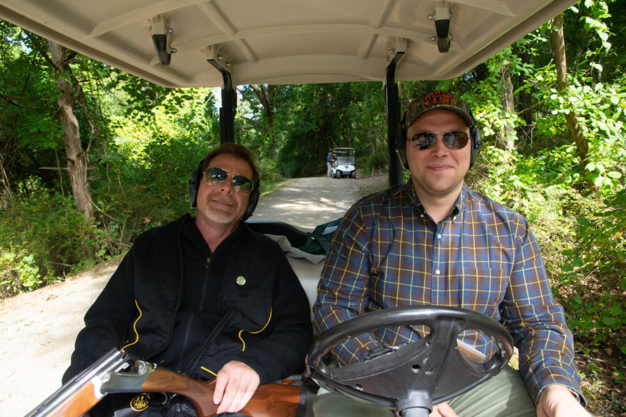 Two men riding golf cart on wooded path