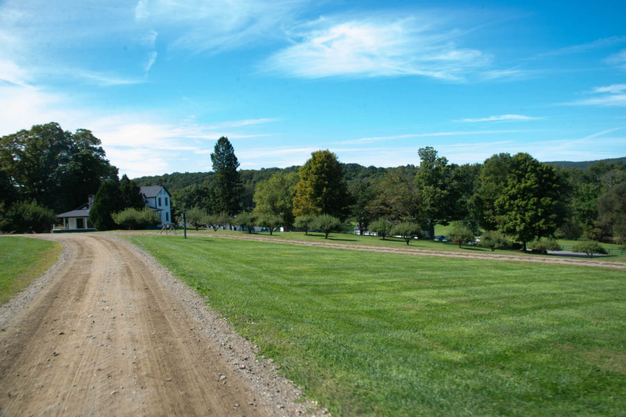 Country dirt road past farmhouse and trees