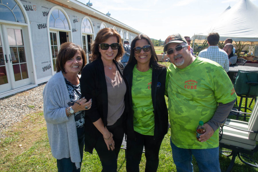 Four adults smiling outdoors at daytime event