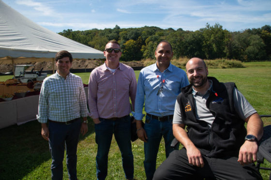 Four men smiling outdoors near a tent.