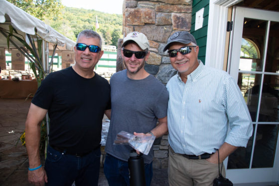 Three smiling men wearing sunglasses outdoors