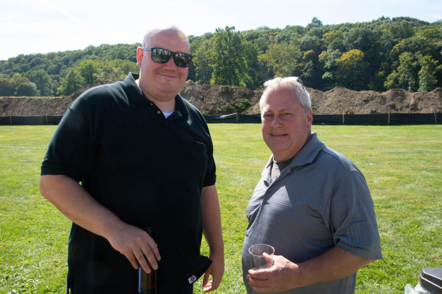 Two men standing on grassy field holding drinks