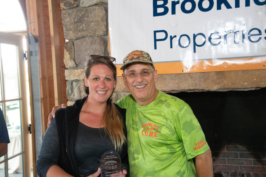 Two smiling people holding award by banner