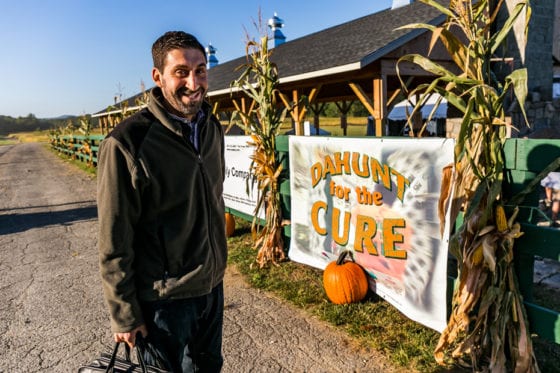 Man smiling beside pumpkin and fundraiser banner