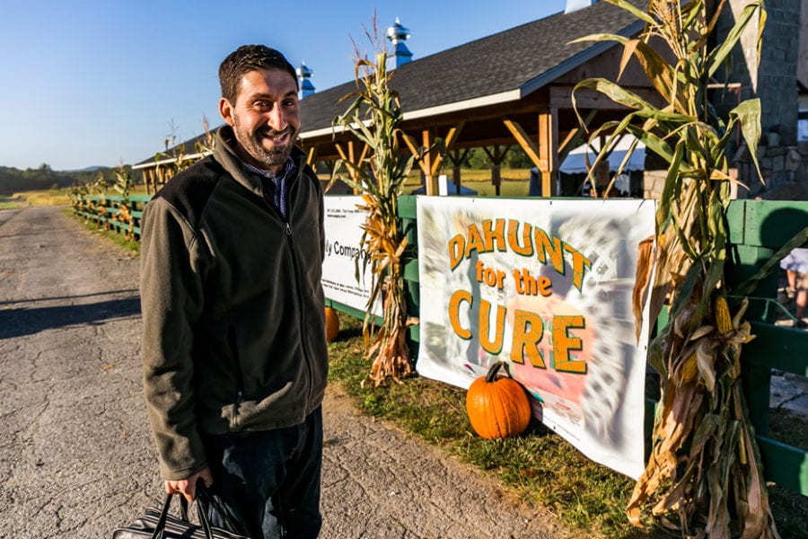 Man smiling beside pumpkin and fundraiser banner