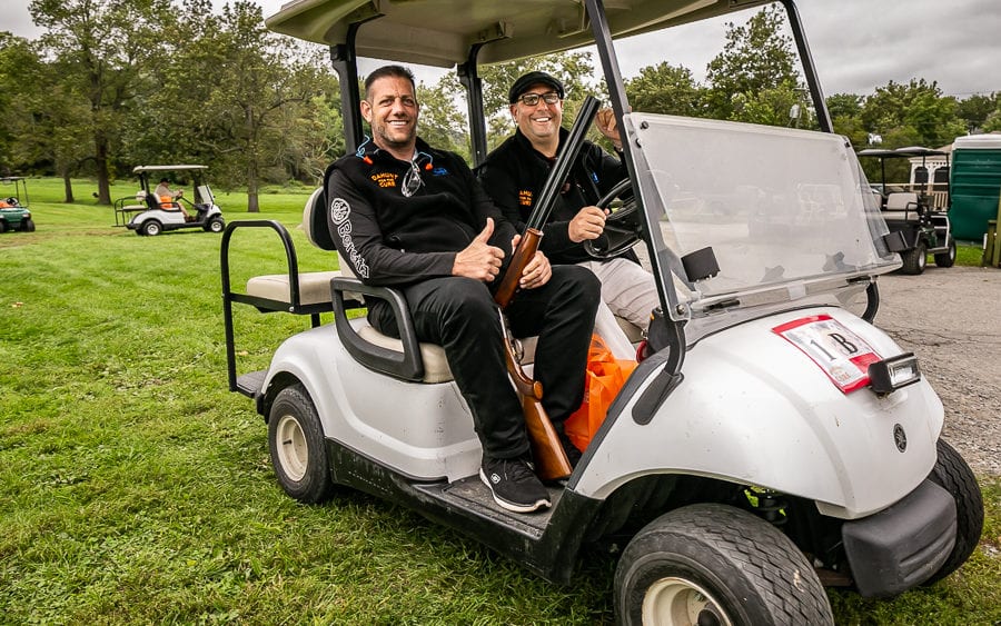 Two men smiling in golf cart holding shotgun