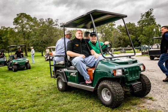 Two men riding green golf cart at park