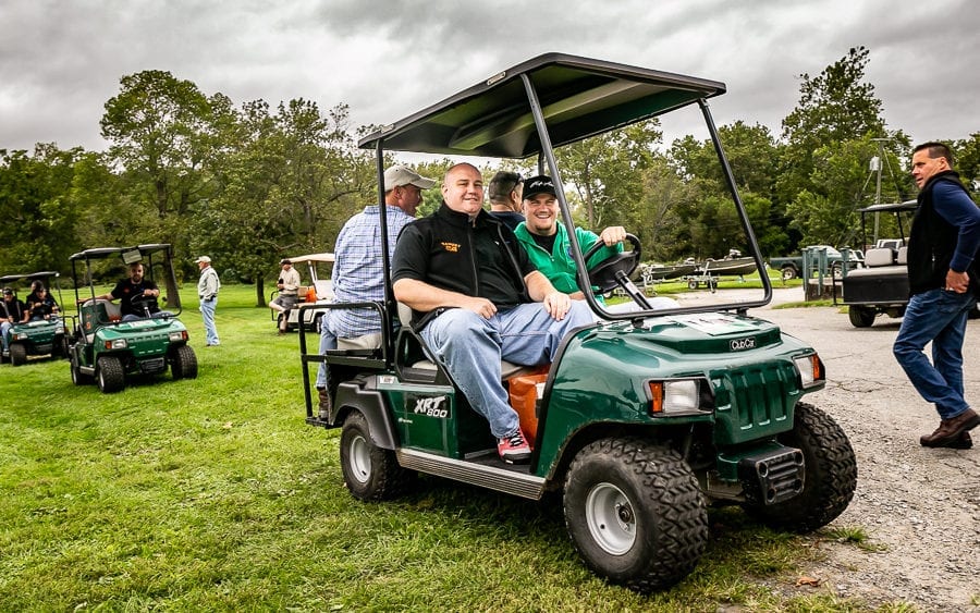 Two men riding green golf cart at park