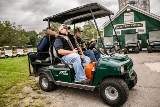 Two men in green utility cart with shotgun