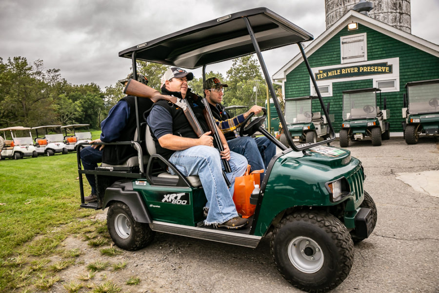 Two men in green utility cart with shotgun
