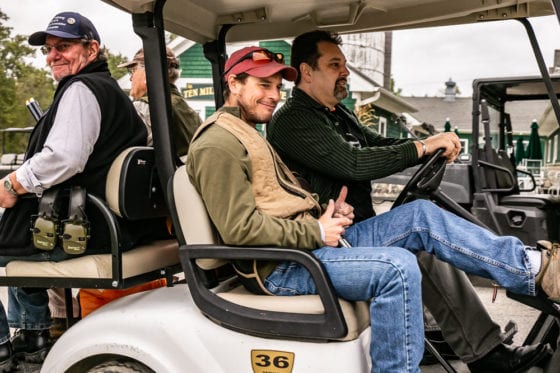 Three men smiling in golf cart outdoors