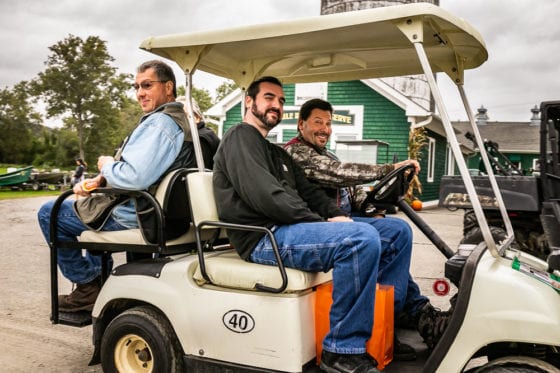 Three men smiling while seated in golf cart