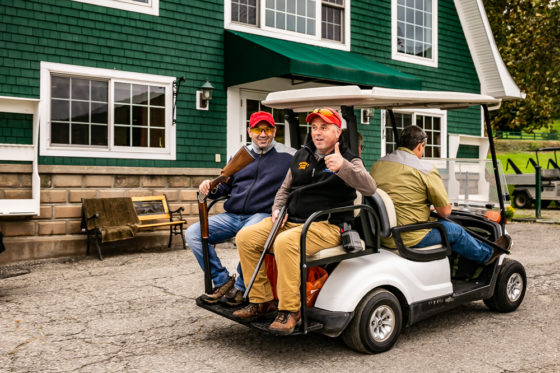 Three golfers riding golf cart by clubhouse