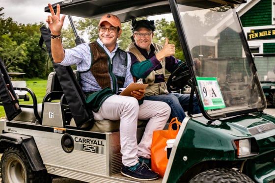 Two men smiling in golf cart peace sign