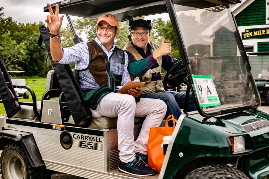 Two men smiling in golf cart peace sign
