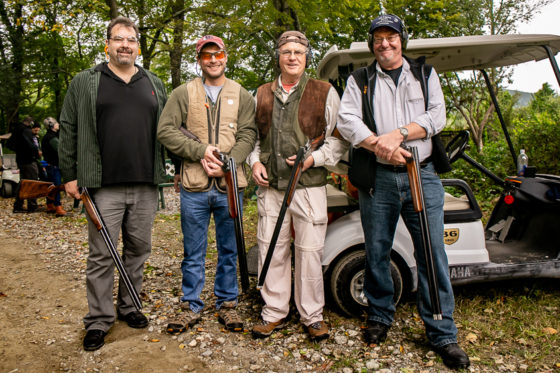 Four men posing with shotguns near golf cart