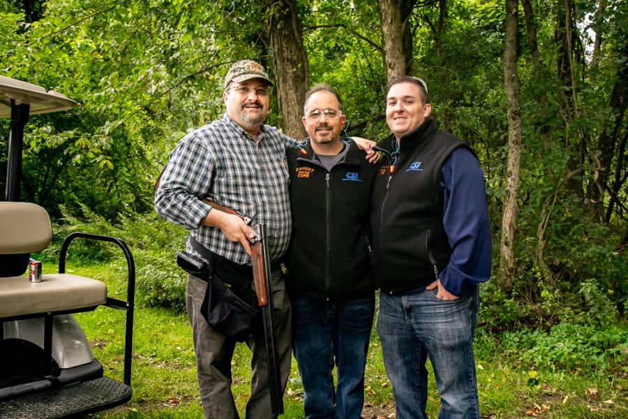 Three men standing in woods, one with shotgun