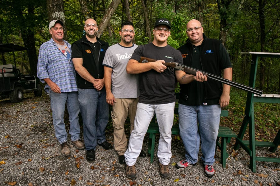 Group of five men outdoors, one holding shotgun