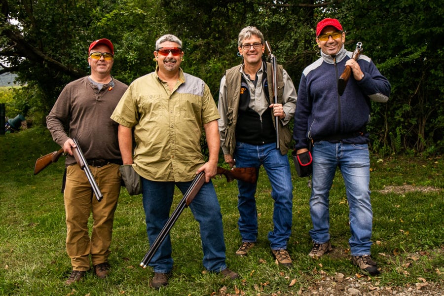 Four men outdoors posing with shotguns