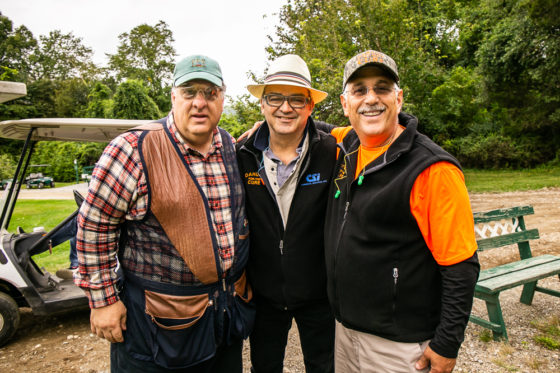 Three men smiling outdoors near golf cart